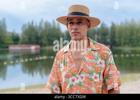 Hispanischer Mann mit Panamahut und hawaiianischem Hemd, gekleidet im lässigen Sommerurlaub-Stil. Er posiert am Strand und zeigt eine entspannte Urlaubsatmosphäre Stockfoto