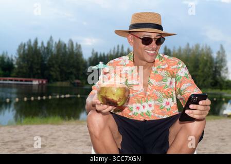 Hispanischer Mann mit Panamahut und hawaiianischem Hemd, gekleidet im lässigen Sommerurlaub-Stil. Er posiert am Strand und zeigt eine entspannte Urlaubsatmosphäre Stockfoto