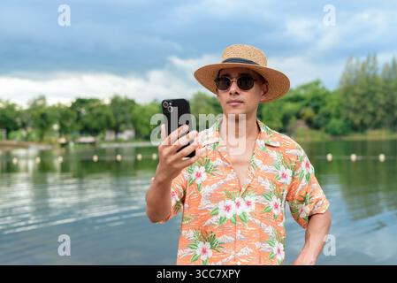 Hispanischer Mann mit Panamahut und hawaiianischem Hemd, gekleidet im lässigen Sommerurlaub-Stil. Er posiert am Strand und zeigt eine entspannte Urlaubsatmosphäre Stockfoto