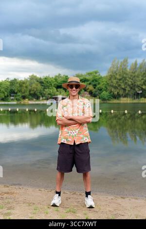 Hispanischer Mann mit Panamahut und hawaiianischem Hemd, gekleidet im lässigen Sommerurlaub-Stil. Er posiert am Strand und zeigt eine entspannte Urlaubsatmosphäre Stockfoto