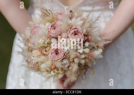Eleganter Hochzeitsstrauß mit roten Rosen, Wildblumen und getrockneten Gräsern in natürlichen Tönen. Ideales Stockbild für Brautkataloge, Hochzeitsplaner Stockfoto