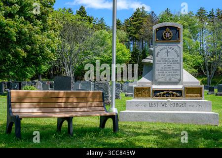 Saint John, NB, Kanada - 21. Juni 2025: Auf einem Friedhof steht ein kanadisches Kriegsdenkmal mit den Worten „OUR HONORED DEAD“ und „LEST WE FORGET“. Eine Parkbank befindet sich neben der Stockfoto