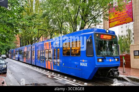 Portland, Oregon – 21. Juni 2025: An einem nassen, bewölkten Tag fährt ein TriMet MAX Stadtzug entlang einer von Bäumen gesäumten Straße im Zentrum der Stadt Stockfoto