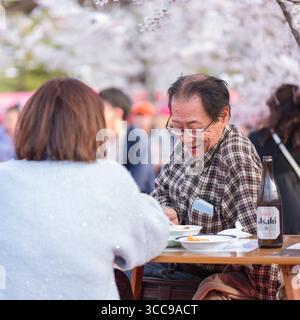 Ein lächelnder reifer Mann sitzt im Freien unter blühenden japanischen Kirschbäumen und speist im Restaurant Hanamijaya Otowa Izakaya, Gionmachi Kitagawa, Higash Stockfoto