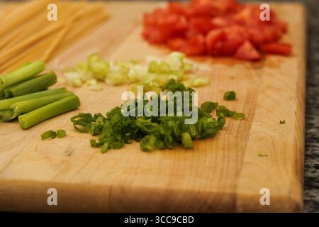 Ungekochte Pasta und frisches Gemüse auf hölzernem Schneidebrett für die Mahlzeitvorbereitung Stockfoto