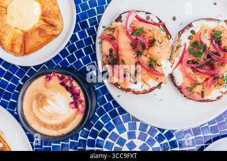 Geräucherte Lachsbagels mit Latte auf blauem Mosaiktisch Stockfoto