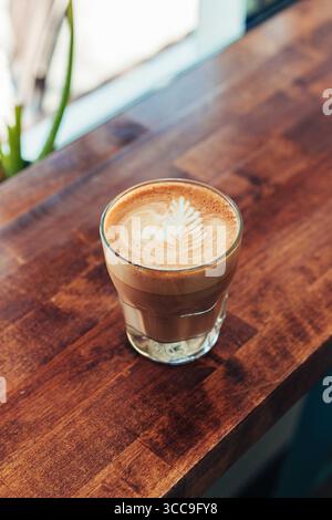 Glas Latte mit Blatt Latte Art auf Holztheke Stockfoto