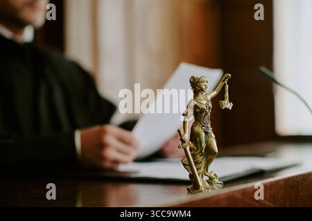 Kaukasischer Richter liest Dokumente hinter der Justizstatue vor Gericht Stockfoto