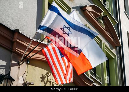 Israelische, polnische und amerikanische Flaggen, die an einer historischen Gebäudefassade unter hellem Tageslicht angebracht sind. Internationale Beziehungen, Kulturdiplomatie, nationale Stockfoto
