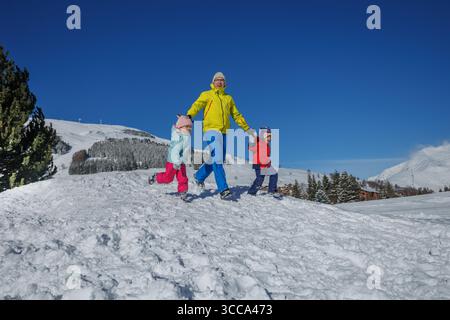 Papa in Neongrün führt zwei Kinder, die über ein verschneite Feld laufen Stockfoto
