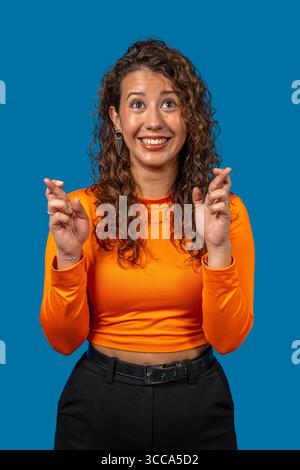 Eine optimistische junge Frau, die sich die Finger drückt und viel Glück wünscht, sich etwas wünscht und auf das Beste hofft Stockfoto