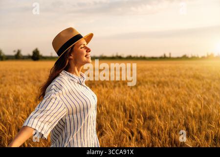 Seitliches Porträt einer glücklichen Frau, die auf dem goldenen Getreidefeld auf dem Land steht Stockfoto