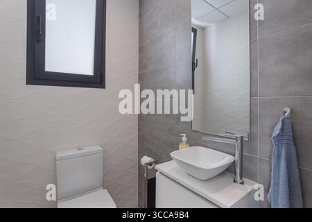 Kleines Badezimmer mit modernem Design, grauen und weißen Fliesen, mattierten Fenstern und einem quadratischen Waschbecken mit Chromarmatur. Stockfoto