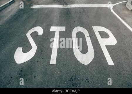 Asphaltierte Asphaltstraße mit Stoppschilder-Aufschrift, die an der Kreuzung gemalt ist, selektiver Fokus Stockfoto