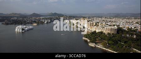 Aus der Vogelperspektive auf den glitzernden Pichola-See, der den unberührten Taj Lake Palace und den grandiosen Stadtpalast, Udaipur, Rajasthan, Indien umschließt. Stockfoto