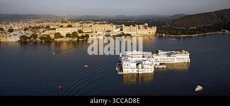Der Blick aus der Vogelperspektive auf das glitzernde Wasser umschließt den weißen Taj Lake Palace und den City Palace Komplex, im Kontrast zu den fernen Hügeln, Udaipur, Rajasthan, Indien. Stockfoto
