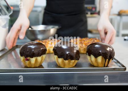 Schokoladenglasierte Rum-Baba-Kuchen auf einem Tablett mit den Händen des Küchenchefs im Rahmen Stockfoto