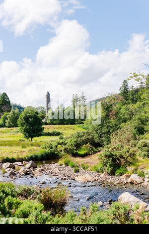 Runder Turm in Glendalough mit Fluss und üppiger grüner Wiese Stockfoto