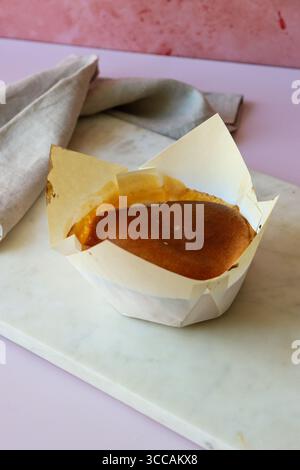 Ein wunderschön gebackener pão-de-ló in einer weißen Pergamentpapierverpackung, ausgestellt auf einer weißen Marmorplatte. Der Kuchen hat ein reichhaltiges, karamellisiertes Oberteil. Stockfoto