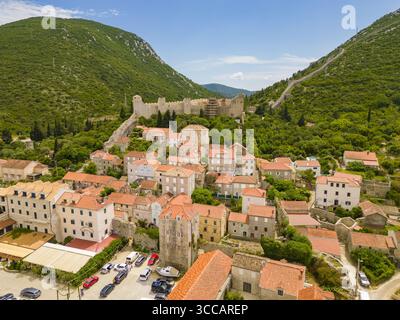Aus der Vogelperspektive auf die historische Stadt eingebettet zwischen grünen Hügeln, gekrönt von alten Steinmauern, wo Terrakottadächer im Kontrast zum üppigen Grün stehen, Mali Ston, Gespanschaft Dubrovnik-Neretva, Kroatien. Stockfoto