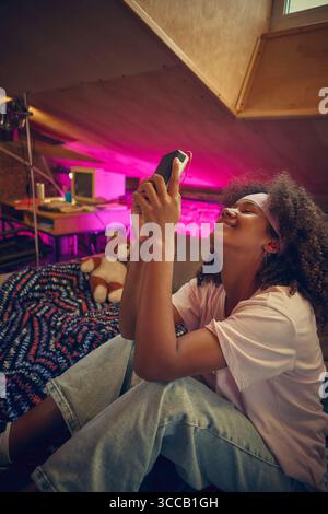 Teenager lächelt, während sie Musik im gemütlichen Retro-Dachgeschoss hört Stockfoto