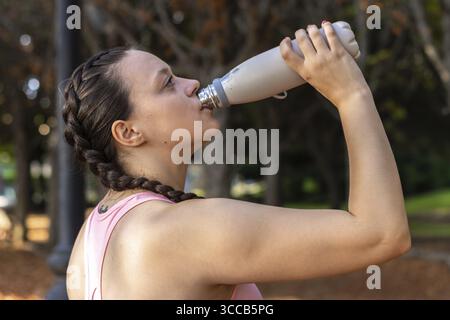 Die Lauferin macht eine Pause, trinkt Wasser während des Laufs im Herbstpark Stockfoto