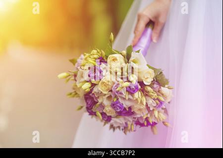 Beauty Hochzeitsstrauß aus violetten und weißen Rosen in Brauthand. Schönheit Sonnenstrahlen Hintergrund Stockfoto