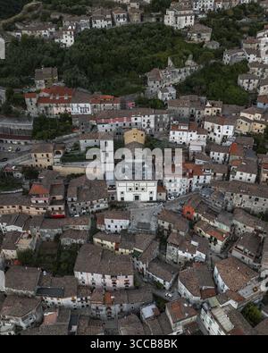 Aus der Vogelperspektive auf dicht gepackte Gebäude mit Terrakottadächern, die um eine zentrale weiße Kirche und einen prominenten Uhrenturm gruppiert sind, Morcone, Benevento, Kampanien, Italien. Stockfoto