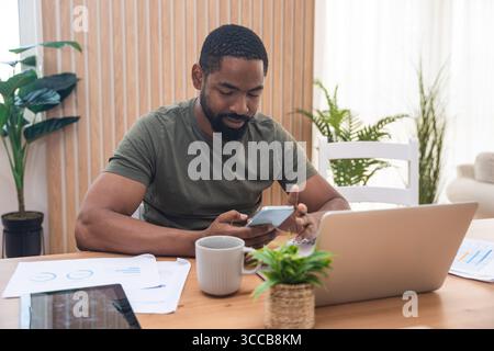 Millennial afroamerikanischer Mann, der sich während eines Webinars oder eines Geschäftstreffens Notizen macht, Laptop benutzt, online arbeitet oder studiert, zuhause am Schreibtisch sitzt Stockfoto
