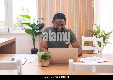 Millennial afroamerikanischer Mann, der sich während eines Webinars oder eines Geschäftstreffens Notizen macht, Laptop benutzt, online arbeitet oder studiert, zuhause am Schreibtisch sitzt Stockfoto