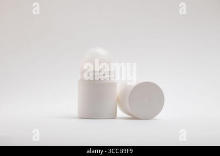 Eine weiße, nicht etikettierte Roll-on-Deodorant-Flasche steht aufrecht neben dem abgenommenen Verschluss, der horizontal auf einem sauberen, Stockfoto