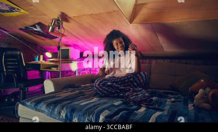 Teenager lächelt an einem kleinen Spiegel im gemütlichen Retro-Dachgeschoss-Schlafzimmer Stockfoto