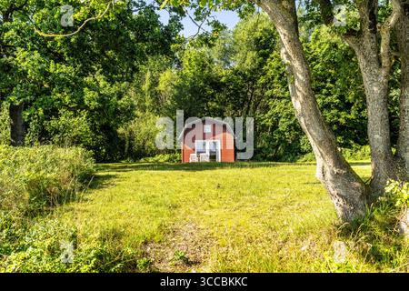 Ein malerisches Backsteinhaus ist von üppigen grünen Hecken umgeben, mit einem malerischen Wald, der im Hintergrund fasziniert und Charme, Gelassenheit und Landschaft weckt Stockfoto