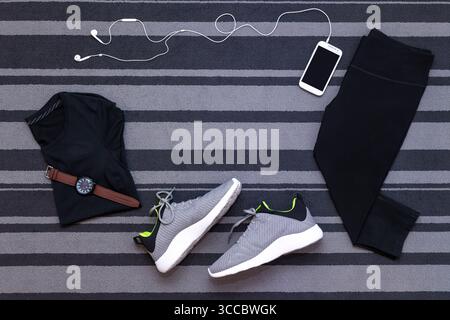 Draufsicht von Laufschuhen, Damenbekleidung, Hosen Strumpfhosen, Smartphone-Run-Anwendung isoliert auf grauem Teppich. Stockfoto