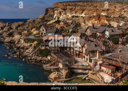 Mit Blick auf Popeye Village in Anchor Bay, Malta, an einem sonnigen Tag mit hellblauem Himmel und einem farbenfrohen Dorf mit Filmkulisse und Küste. Stockfoto