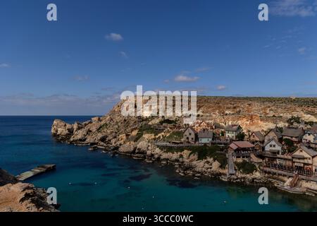 Mit Blick auf Popeye Village in Anchor Bay, Malta, an einem sonnigen Tag mit hellblauem Himmel und einem farbenfrohen Dorf mit Filmkulisse und Küste. Stockfoto