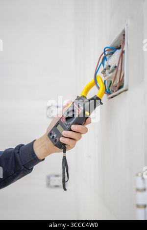 Hände eines Elektrikers zur Messung des elektrischen Stroms mit einem Amperemeter. Stockfoto