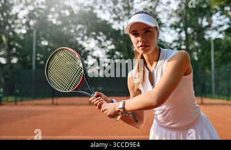 Fokussierte Frau in weißer Sportswear, die sich auf einen Rückhandschuss während des Tennisspiels vorbereitet. Konzept: Entschlossenheit, sportliche Disziplin, Fokus in Aktion. Stockfoto