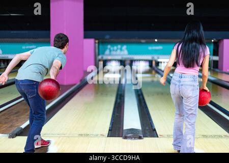 Rückansicht von zwei Freunden, die Bowlingbälle werfen, Spaß haben und ihr gemeinsames Wochenende in einem Bowlingclub genießen Stockfoto