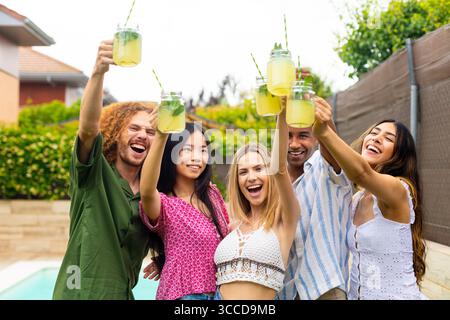 Gruppe von fröhlichen, ethnischen Freunden, die mit hausgemachter Limonade anstoßen, genießen Sommerparty am Pool Stockfoto