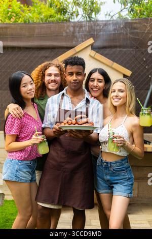 Verschiedene Freunde lächeln und halten gegrilltes Essen und Limonade und genießen gemeinsam eine Grillparty im Hinterhof Stockfoto