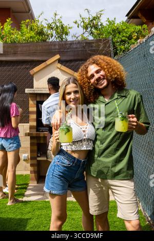 Junges Paar genießt erfrischende Limonade bei einer Grillparty im Hinterhof mit Freunden und feiert den Sommer mit guter Gesellschaft und leckerem Essen Stockfoto