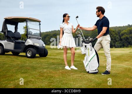 Ein Paar genießt eine gute gemeinsame Zeit auf dem Golfplatz, lacht und tauscht seine Golfausrüstung aus, was die wunderschöne Atmosphäre hervorhebt Stockfoto