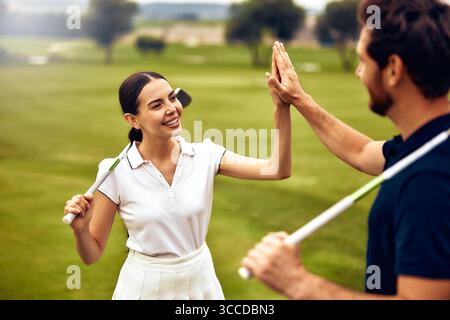 Ein fröhliches Paar genießt einen sonnigen Tag auf dem malerischen Golfplatz und feiert mit Begeisterung einen perfekt ausgeführten Schuss mit einem fröhlichen High Stockfoto