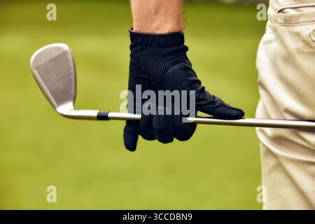 Dieses Bild zeigt eine Nahaufnahme eines Golfers, der einen Eisenklub packt, und zeigt einen schwarzen Handschuh, der einen schönen Kontrast zum leuchtenden grünen Hintergrund bildet Stockfoto