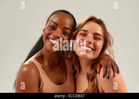 Porträt von zwei fröhlichen, vielseitigen Frauen, die lächeln und umarmen. Afroamerikaner und tätowierte Frau posieren zusammen. Konzept: Freundschaft, Vielfalt, Natur Stockfoto