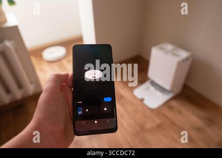 Freiberufler arbeiten, während Roboter-Vakuum den Boden über Smartphone-App steuern und so bequem reinigen Stockfoto