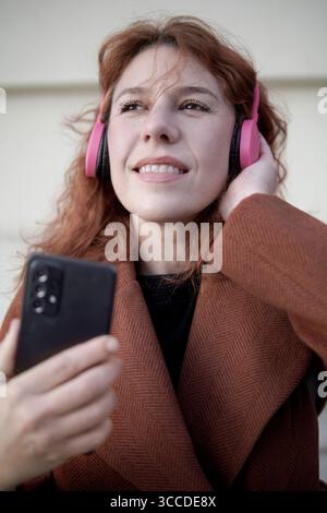 Lächelnde Frau, die Musik hört, während sie ein Smartphone hält Stockfoto