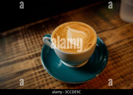 Frisch gebrühter Cappuccino mit schöner Latte Art sitzt auf einem rustikalen Holztisch in einem gemütlichen Café und lädt Kaffeeliebhaber zum Genießen ein Stockfoto