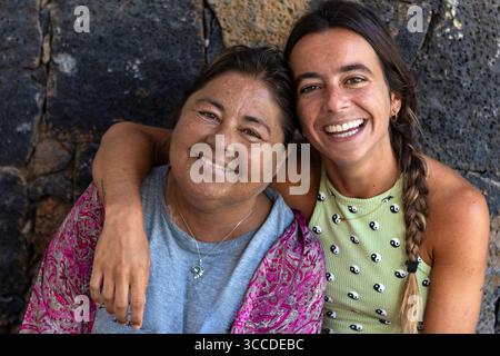 Glückliche Mutter und Tochter lächeln und umarmen sich vor einer Steinmauer Stockfoto